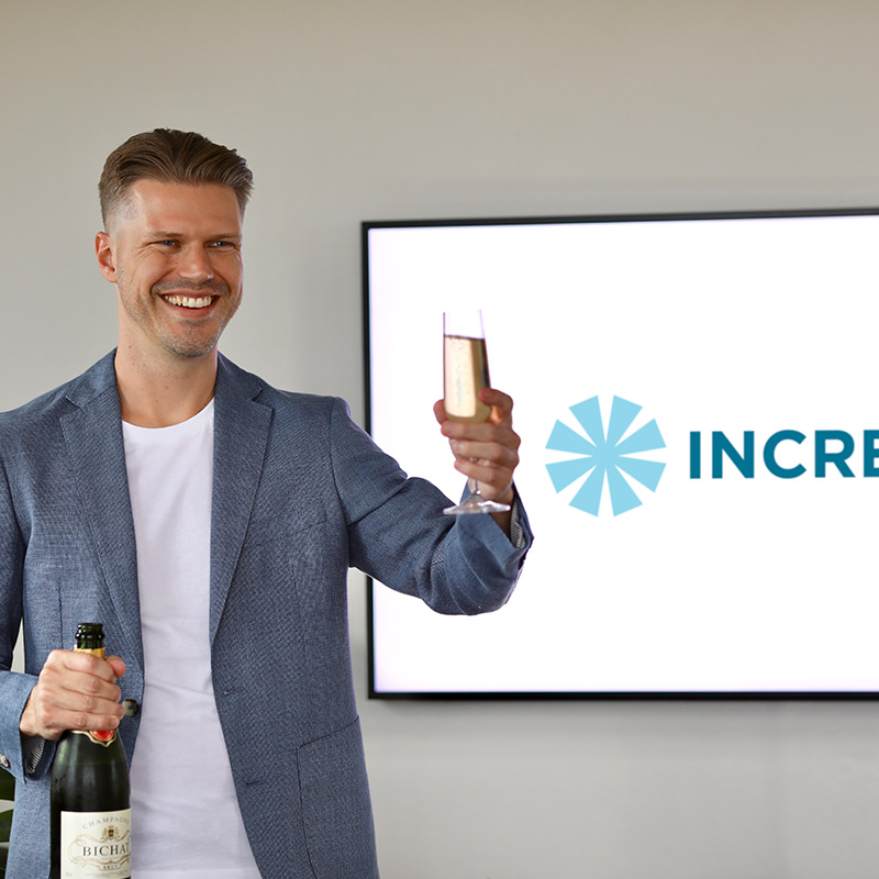 Ariel raising a toast in front of the Increate logo